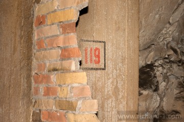 Za rozdrcenou cihlovou příčkou lze spatřit původní číslo místnosti č. 119.