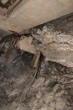Rozlámané, železobetonové nosníky stropu jsou obklopeny směsí mokrého jílu a kamení.