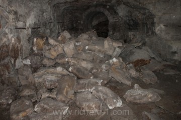 Rozházené hromady ztvrdlých pytlů vápna a cementu v chodbě č. 12.